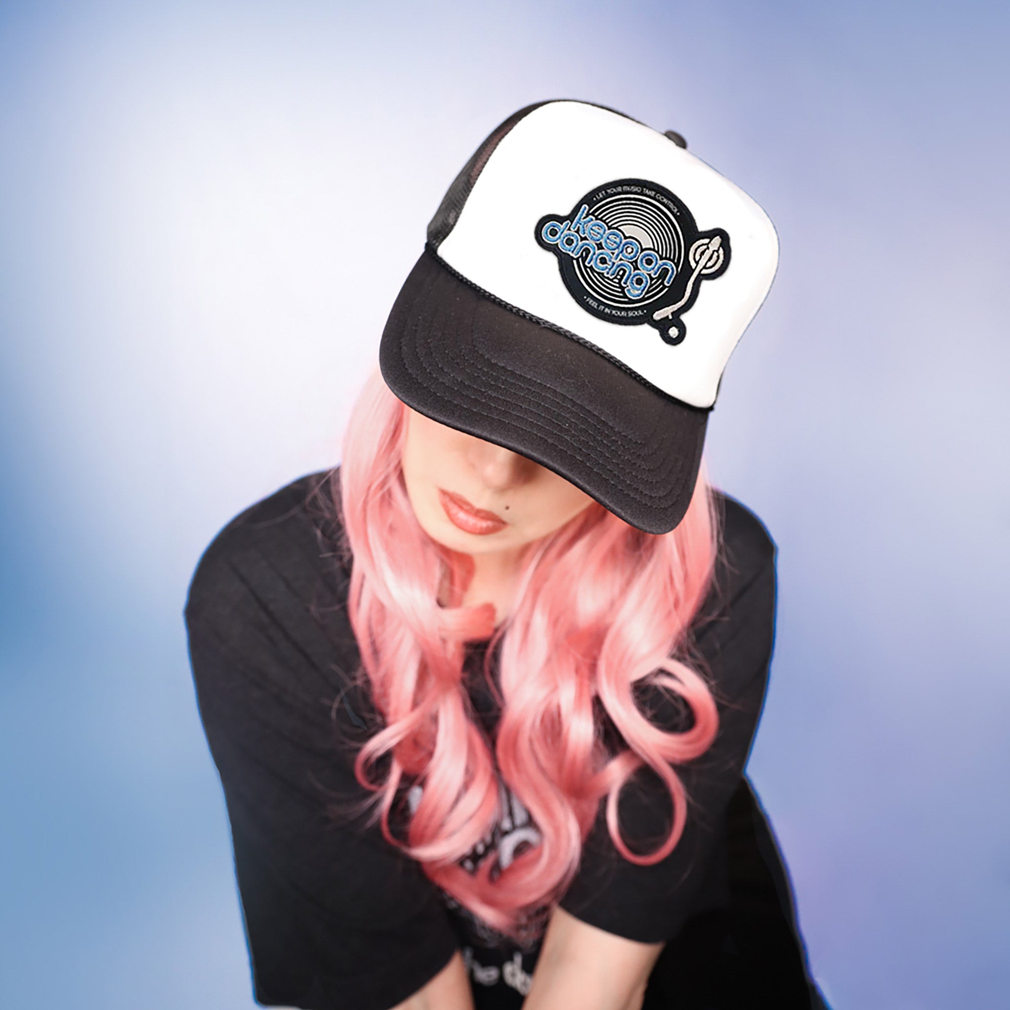 Celleste Keep on Dancing Trucker hat with embroidered black, white and blue patch. White hat, black beak, front view on model.